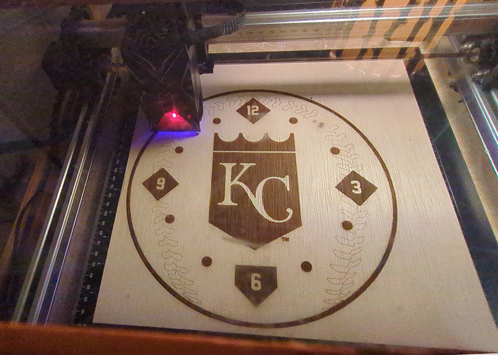 Laser cutter engraving a Kansas City clock face into wood