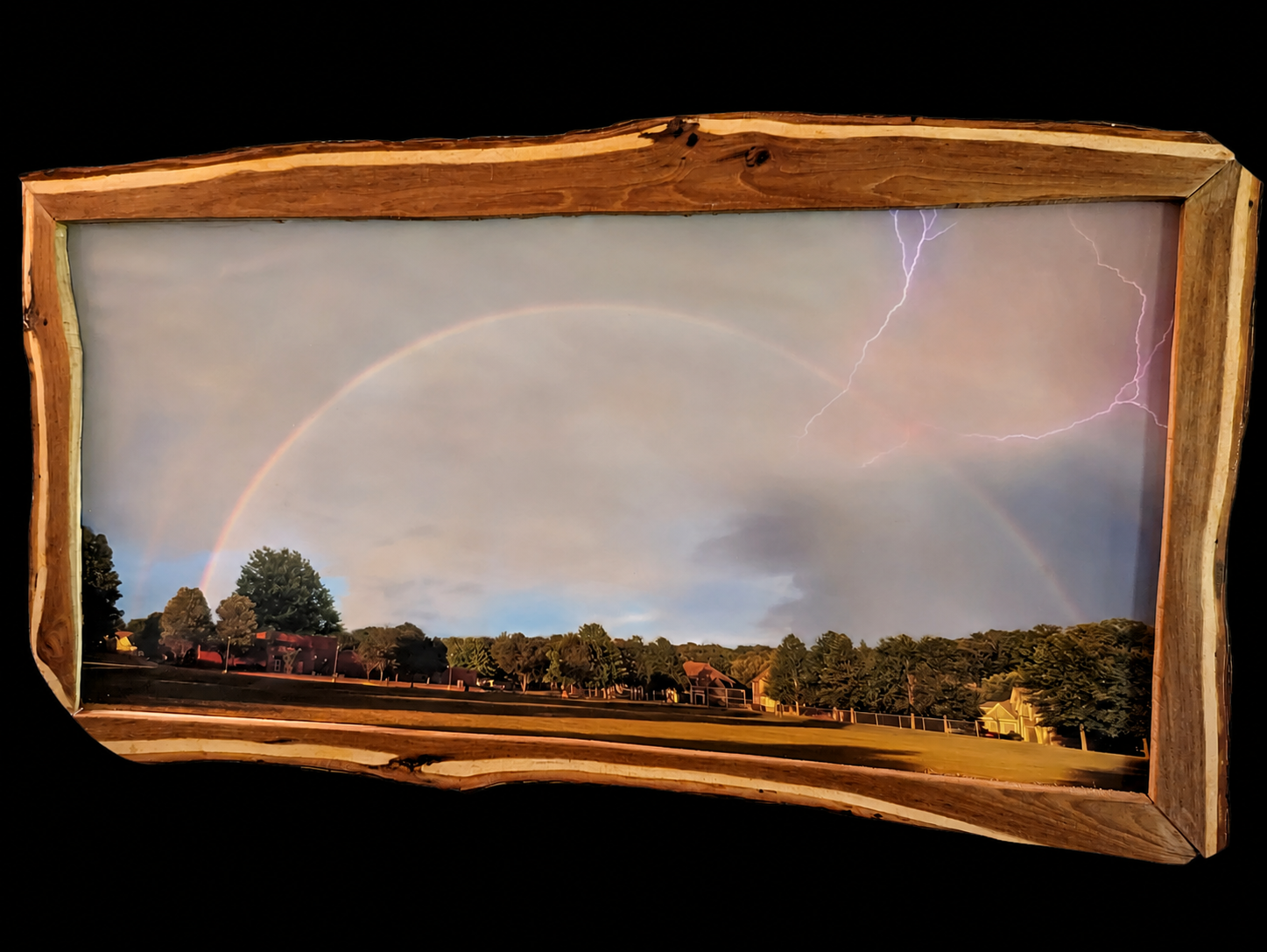 A live-edge wooden frame against a black background, holding a photograph of a rainbow and lightning